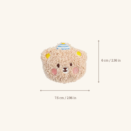 A small plush bear-shaped accessory centered on a light warm beige background, with measurement arrows and text showing dimensions of 7.5 cm by 6 cm.