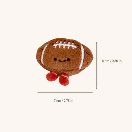 A small plush football-shaped toy with a stitched face and red feet, shown on a light beige background with dimension arrows and text indicating 7 cm by 6 cm.