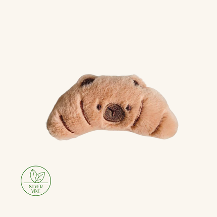 A plush, crescent-shaped dog toy in a light tan or beige color with embroidered dark brown eyes, nose, and mouth, shown on a solid off-white background with a 'Silver Vine' brand logo in the bottom-left corner.