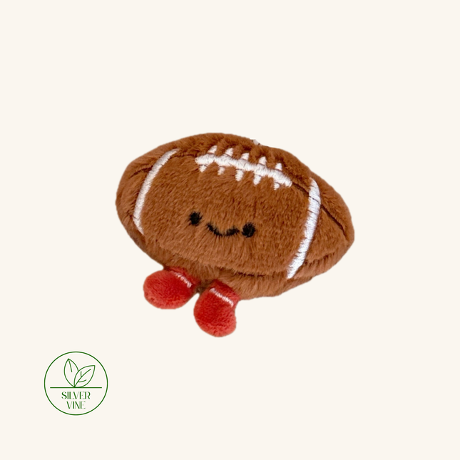 A brown plush football toy with embroidered white laces, a smiling face, and small red feet, shown on a plain light beige background. A Silver Vine logo appears in the lower-left corner.